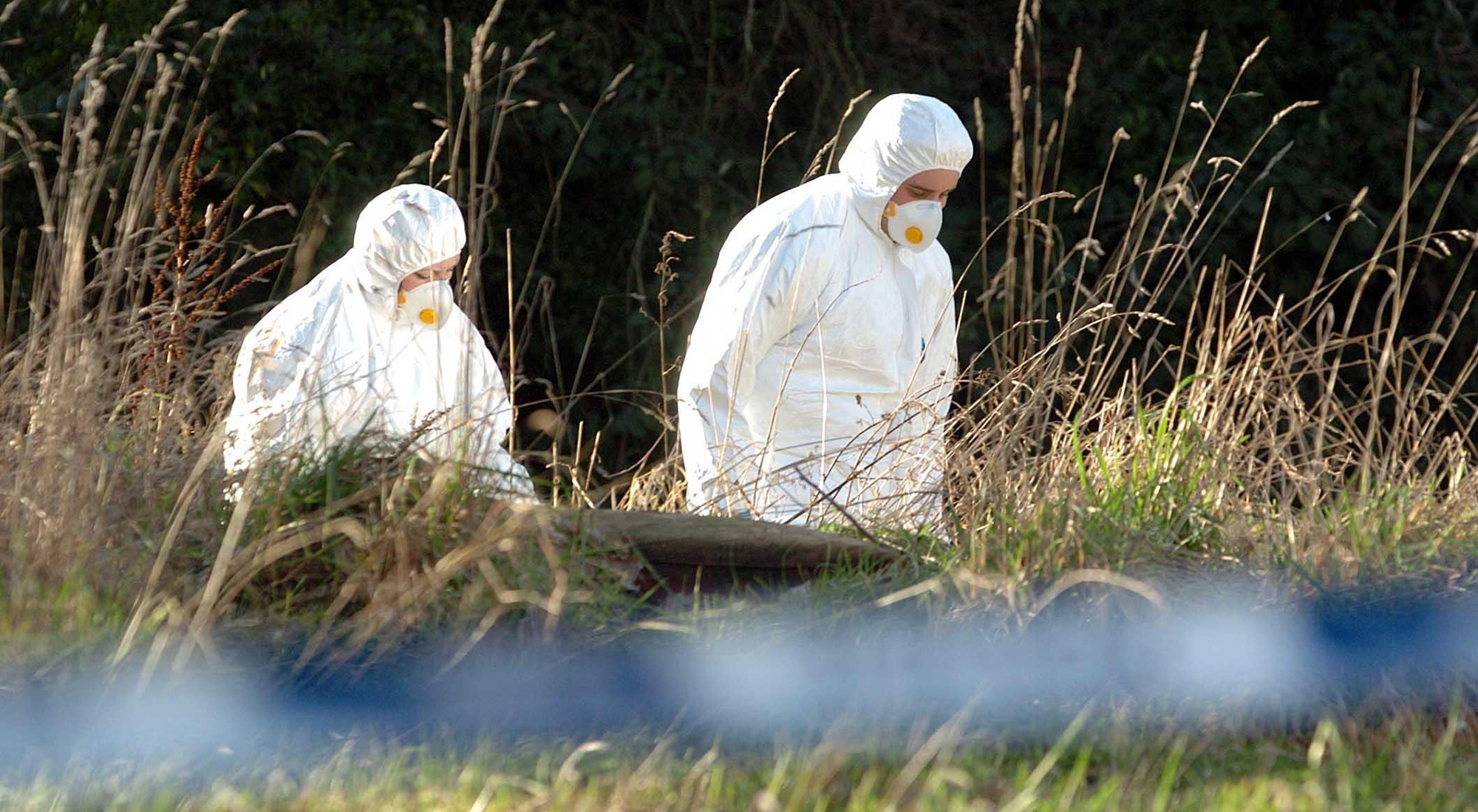 Two people in hazmat suits in a field