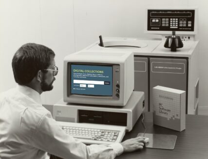 man in glasses sitting in front of a computer screen holding a mouse