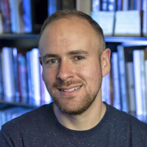 Roland Betancourt in front of a blue-lit bookshelf