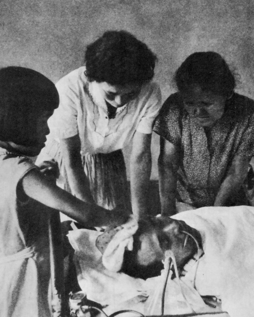 Two women and a girl gather around a man in a hospital bed