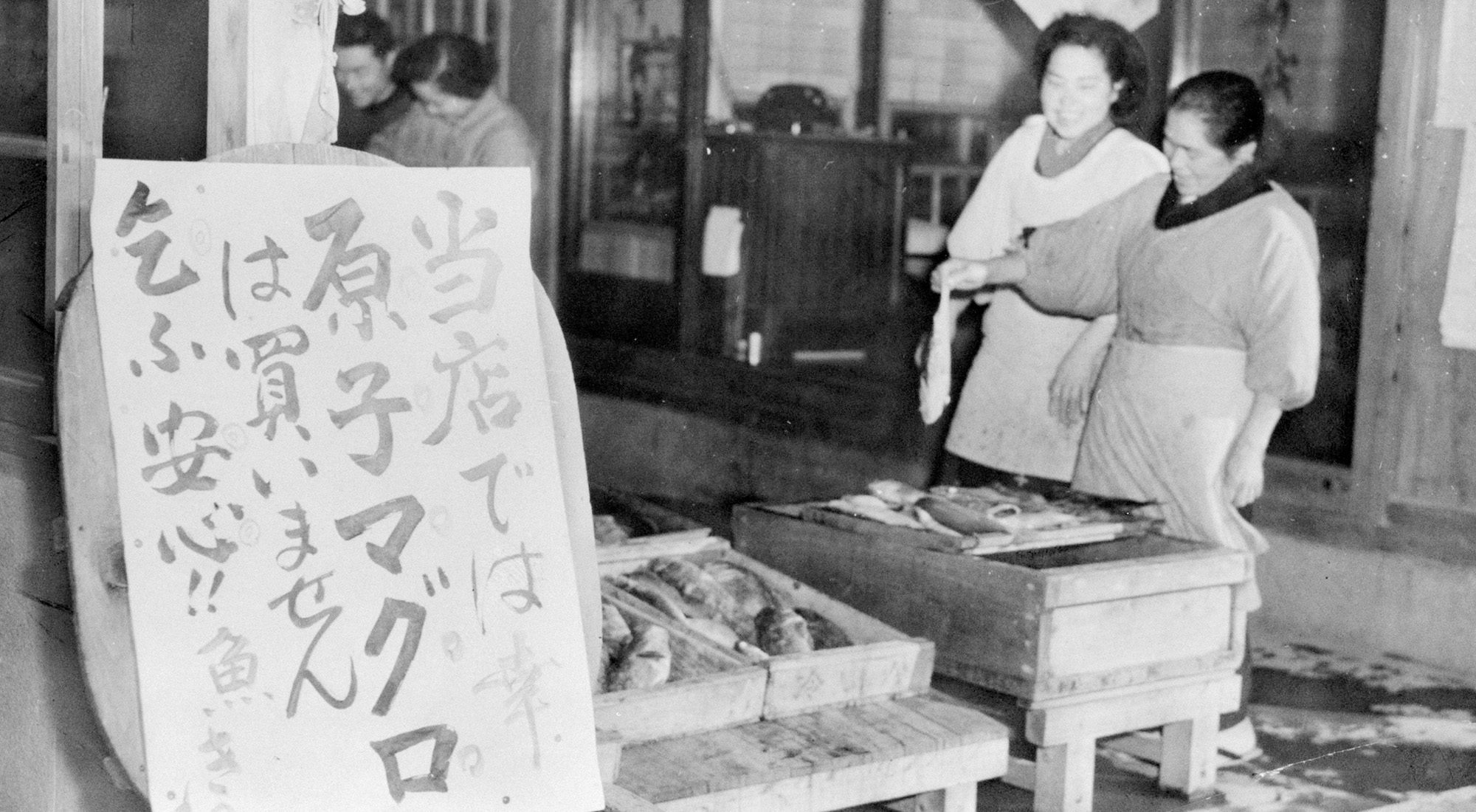A table with crates of fish and a sign written in Japanese characters