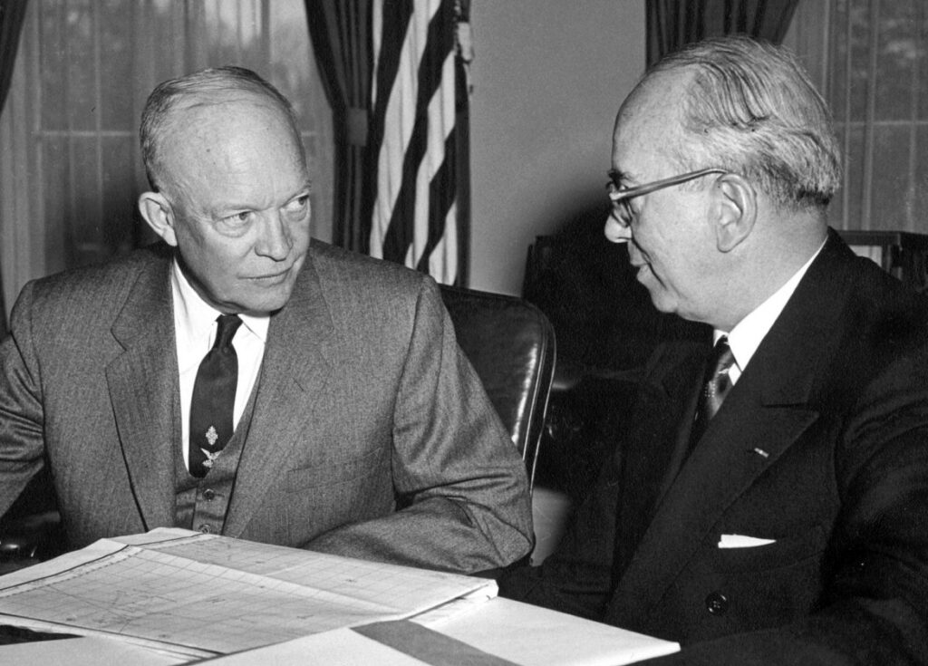Two men sitting at a desk with an American flag in the background