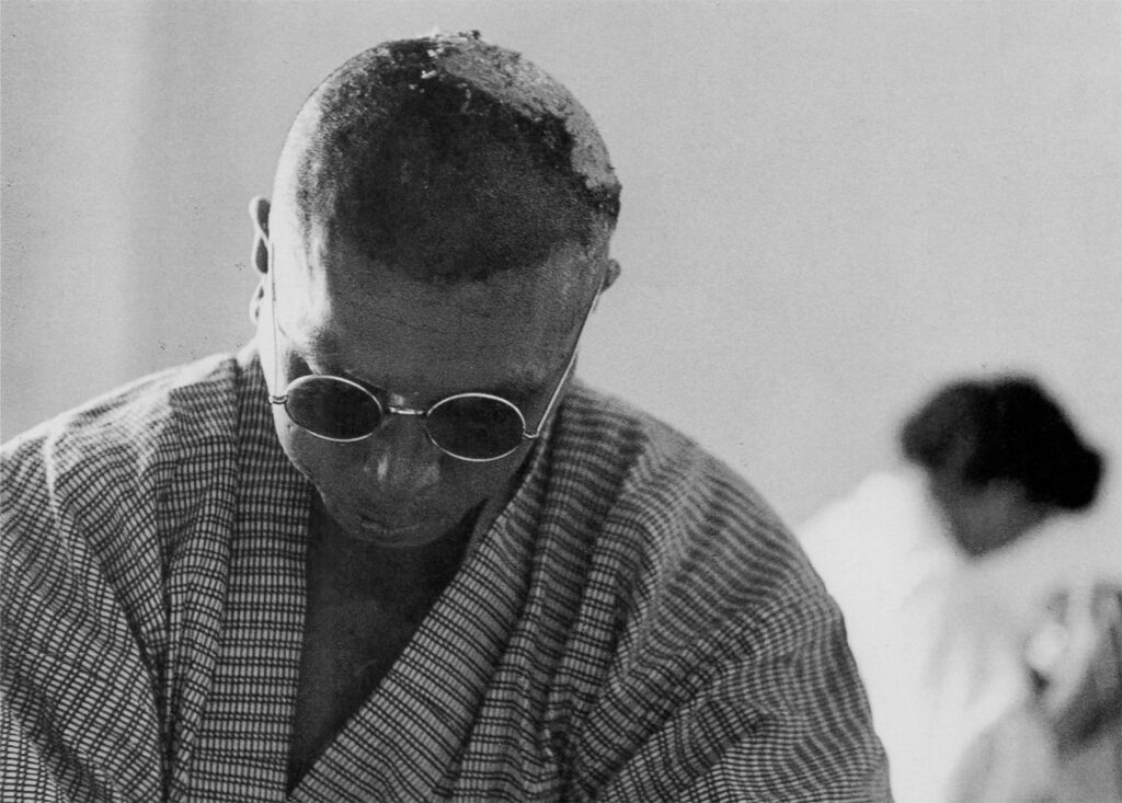 A man wearing sunglasses and a robe with his face titled downward