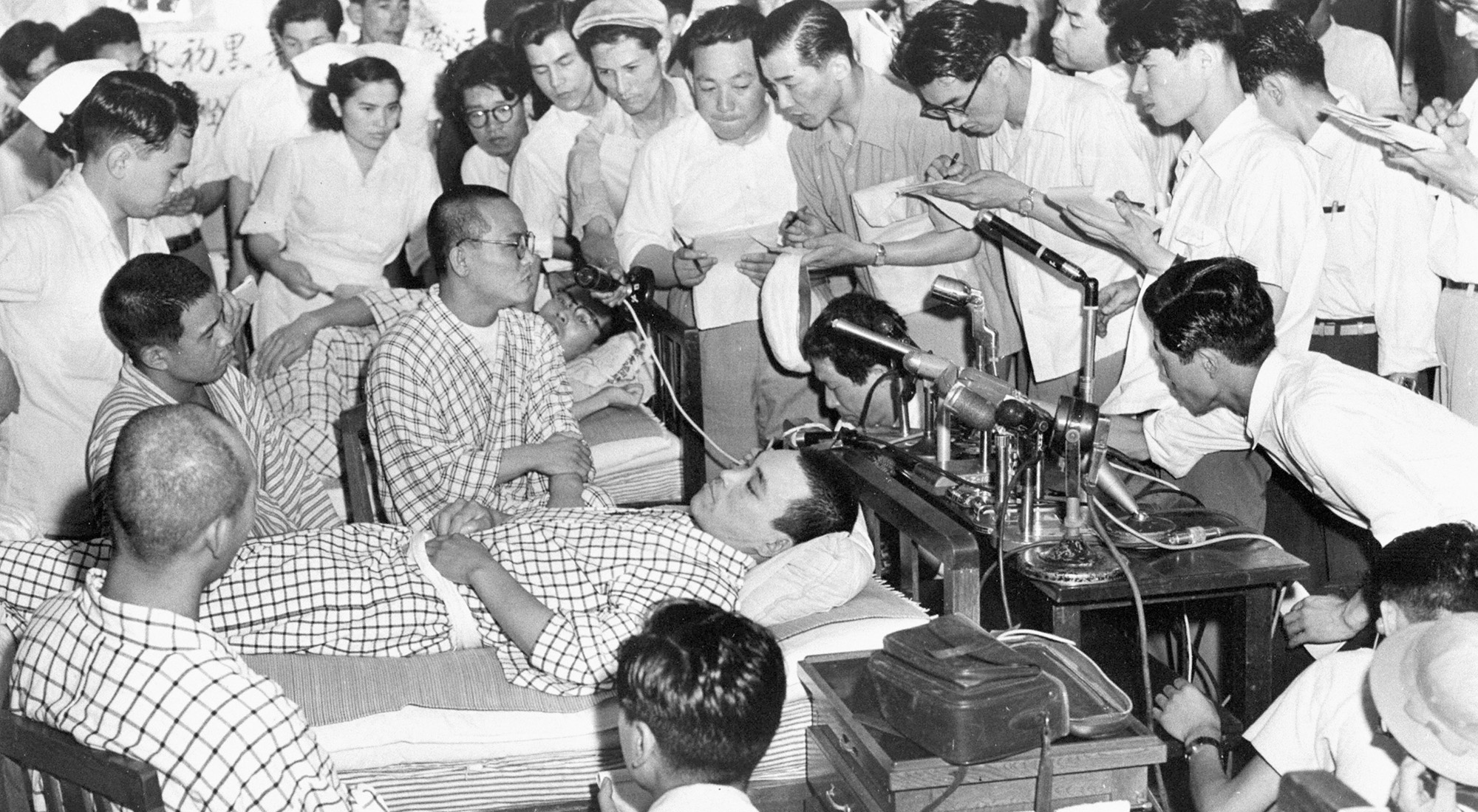 A large group of people gathered around two men in robes on hospital beds