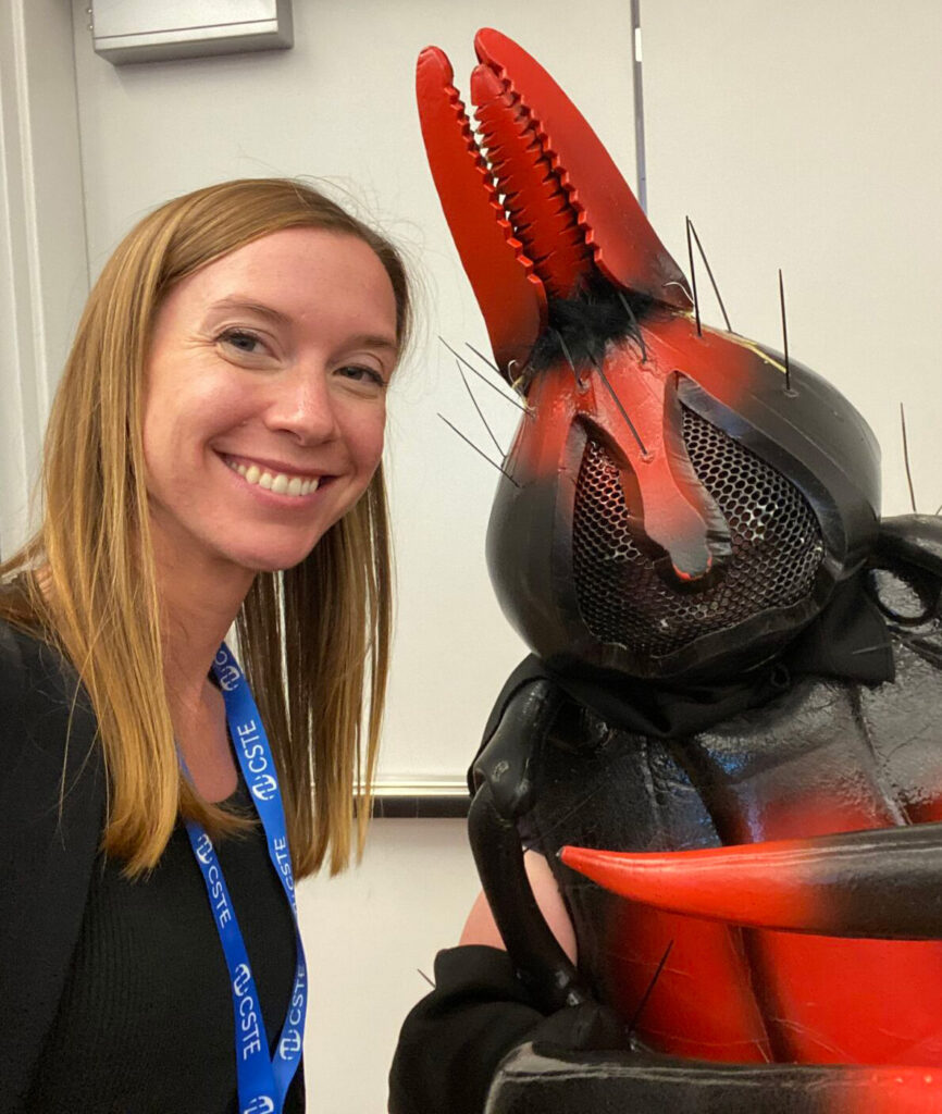 A smiling woman posing with a person in a tick costume