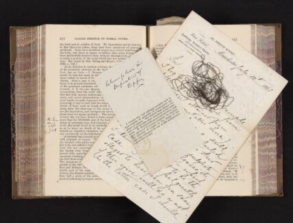old book with newspaper clipping, wire, and handwritten notes on top of pages