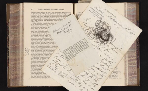 old book with newspaper clipping, wire, and handwritten notes on top of pages