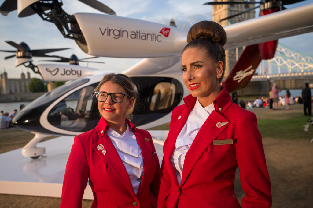 Two women in red clothing standing next to a small aircraft.