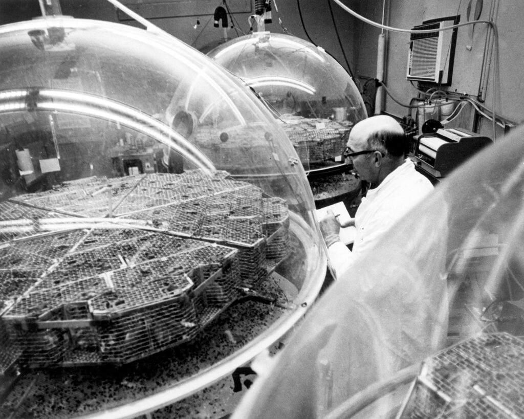 Man in a white lab coat surrounded by rounded plastic enclosures.