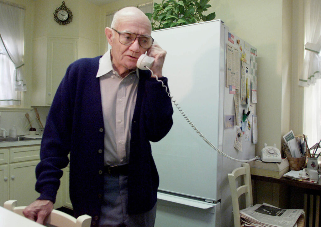 A man in a kitchen talking on a telephone