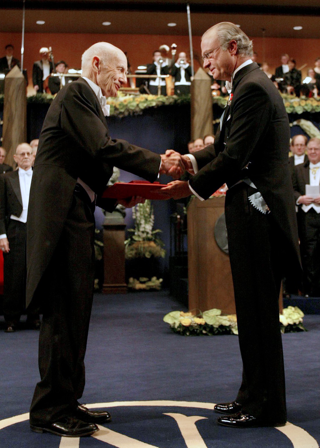 Two men in formal wear shaking hands on a stage