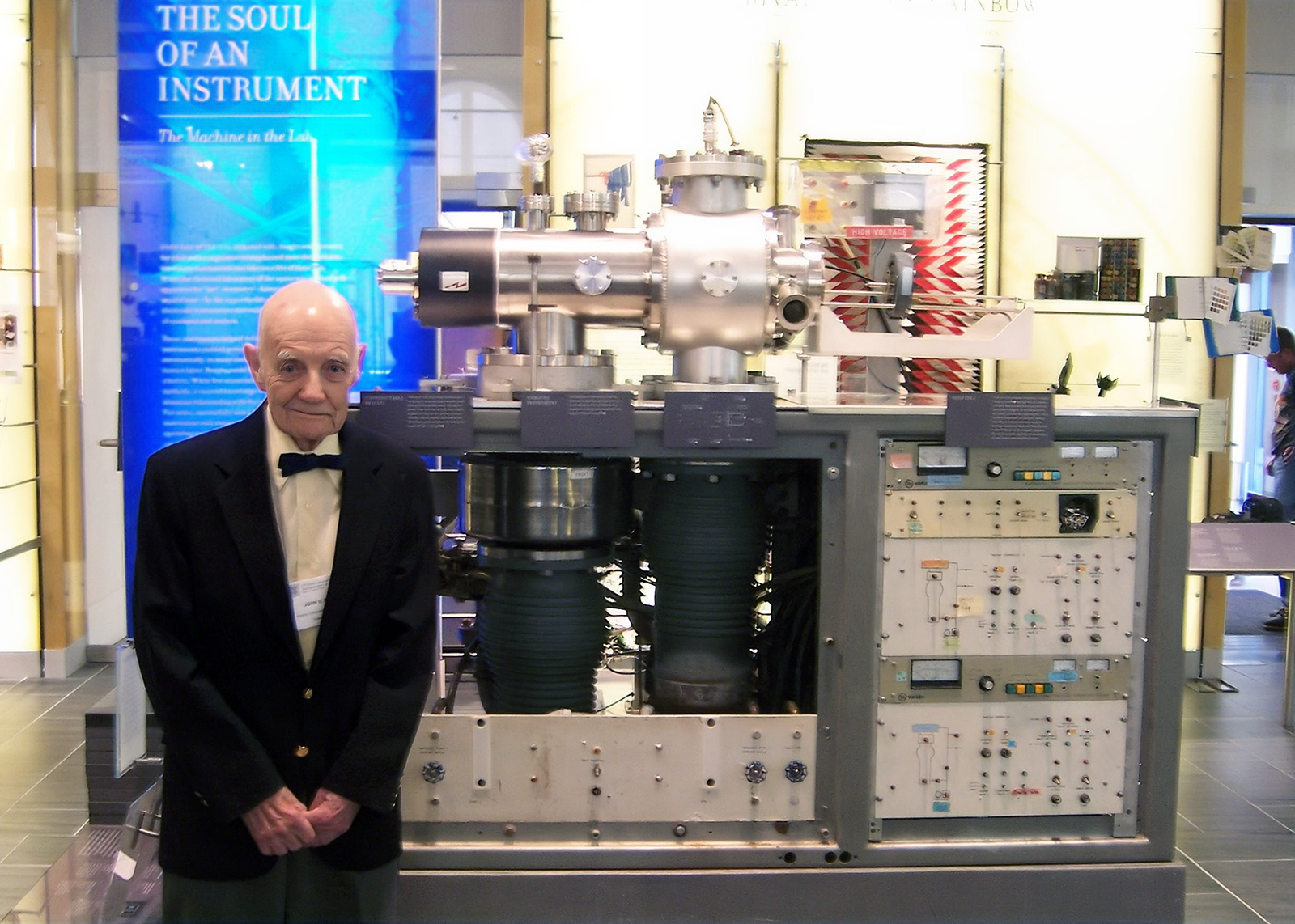 A man in a suit standing next to a large machine in a museum
