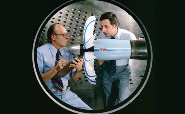 Two men standing next to a plane propeller in a room with metal walls.