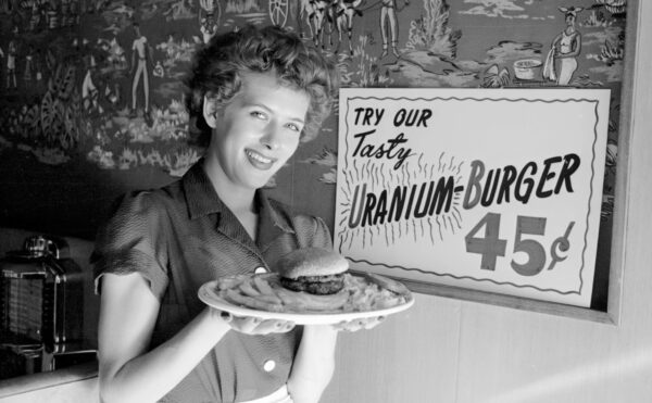 Woman holding a plate containing a hamburger and fries. A sign behind her reads: “Try our tasty uranium-burger.”