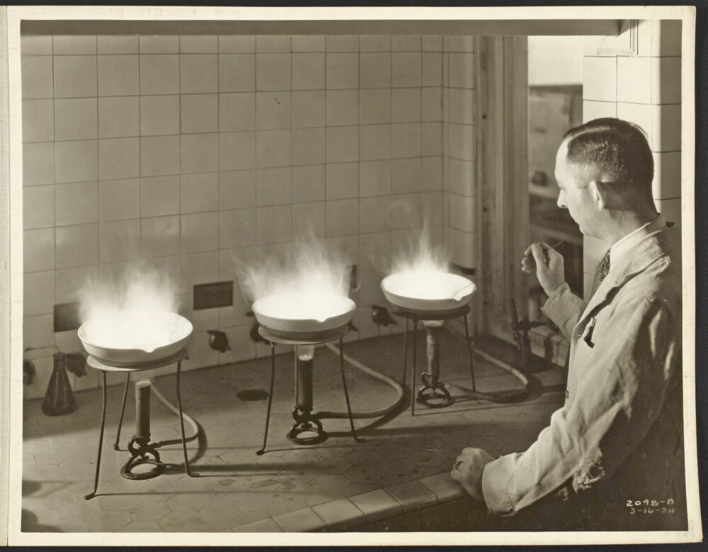 photograph of a man, seen from behind, working with Bunsen burners