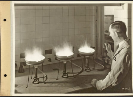 photograph of a man, seen from behind, working with Bunsen burners