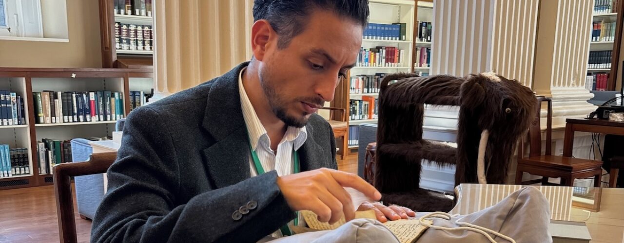 man sitting at a table in a library looking at a book