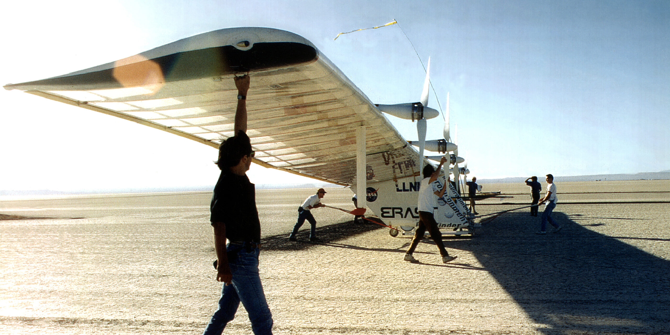 A group of men pushing a plane on a dry lakebed.