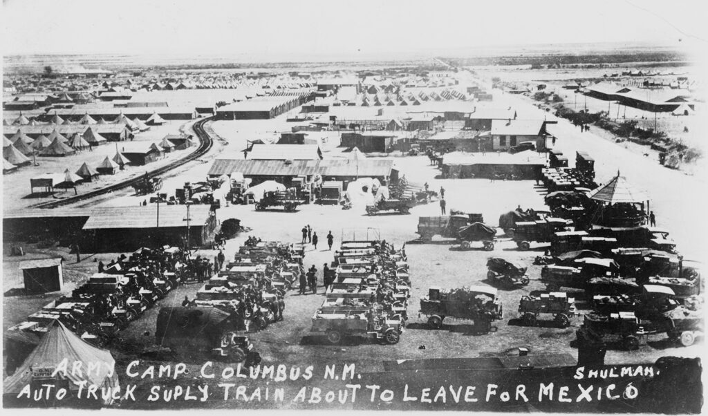 A photograph of trucks, tents, and buildings. A caption at the bottom reads: “Army camp Columbus N.M. / Auto truck suply [sic] train about to leave for Mexico / Shulman” 