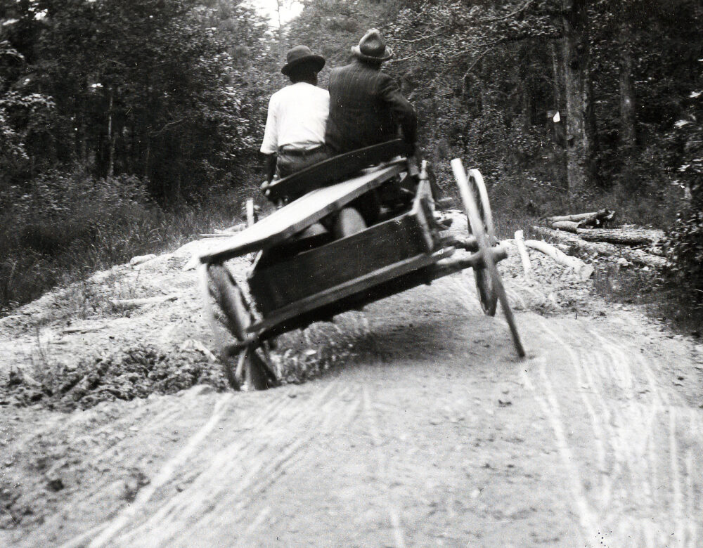 Two men riding in a wagon on a road with deep holes.