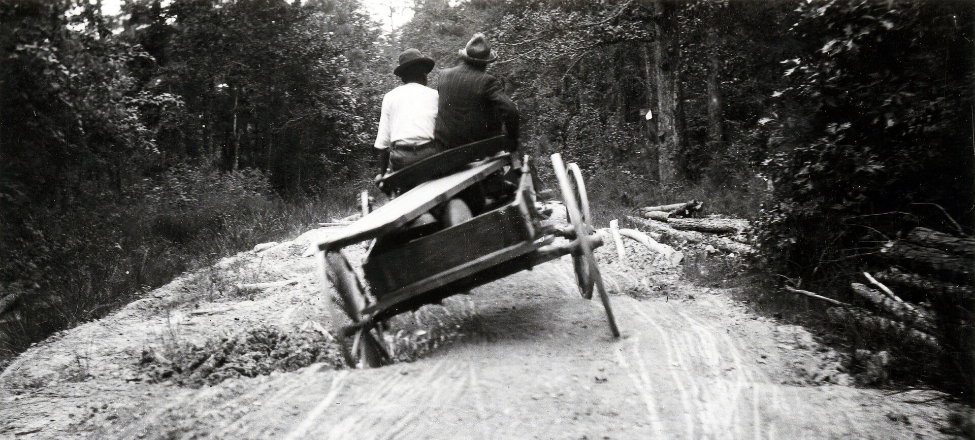 Two men riding in a wagon on a road with deep holes.