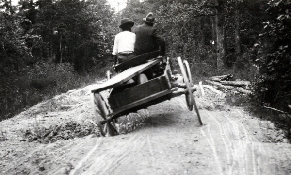 Two men riding in a wagon on a road with deep holes.