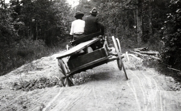 Two men riding in a wagon on a road with deep holes.