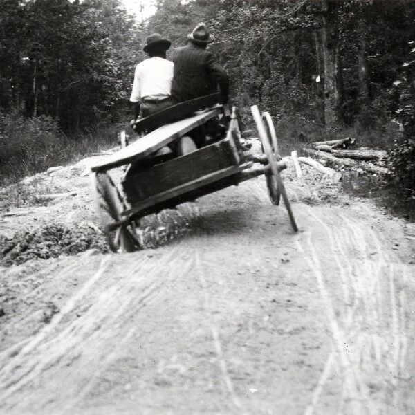 Two men riding in a wagon on a road with deep holes.