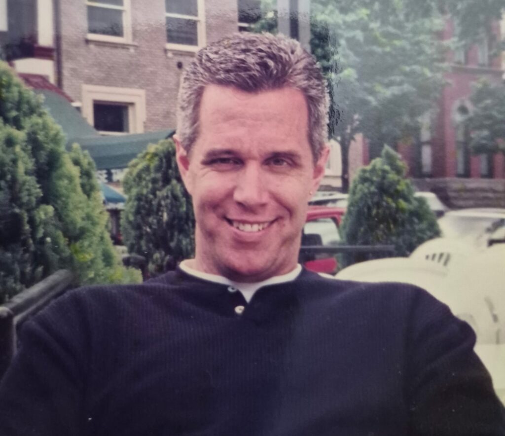 man wearing blue sweater sitting outside smiling