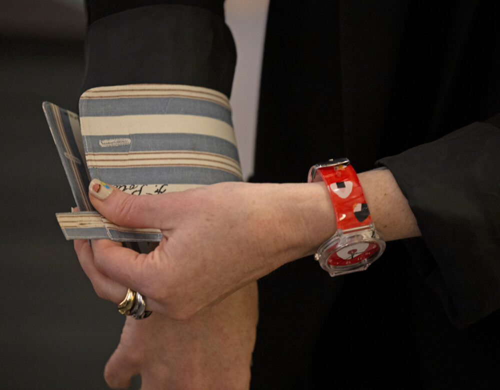 left hand, wearing a ring and a watch with a red band featuring an onigiri rice ball pattern, fastening a striped dress shirt cuff